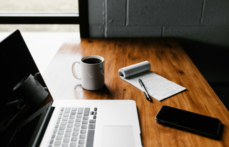 Laptop with notepad and cup of coffee next to it